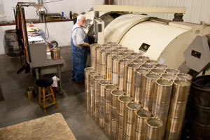 achinist stands beside a large machine with rows of bronze bearing sleeves staged for production.