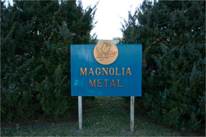 Magnolia Metal monument sign with bronze logo set in front of evergreen landscaping.