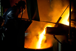 Molten metal pours in a bright stream into a container during a foundry operation.