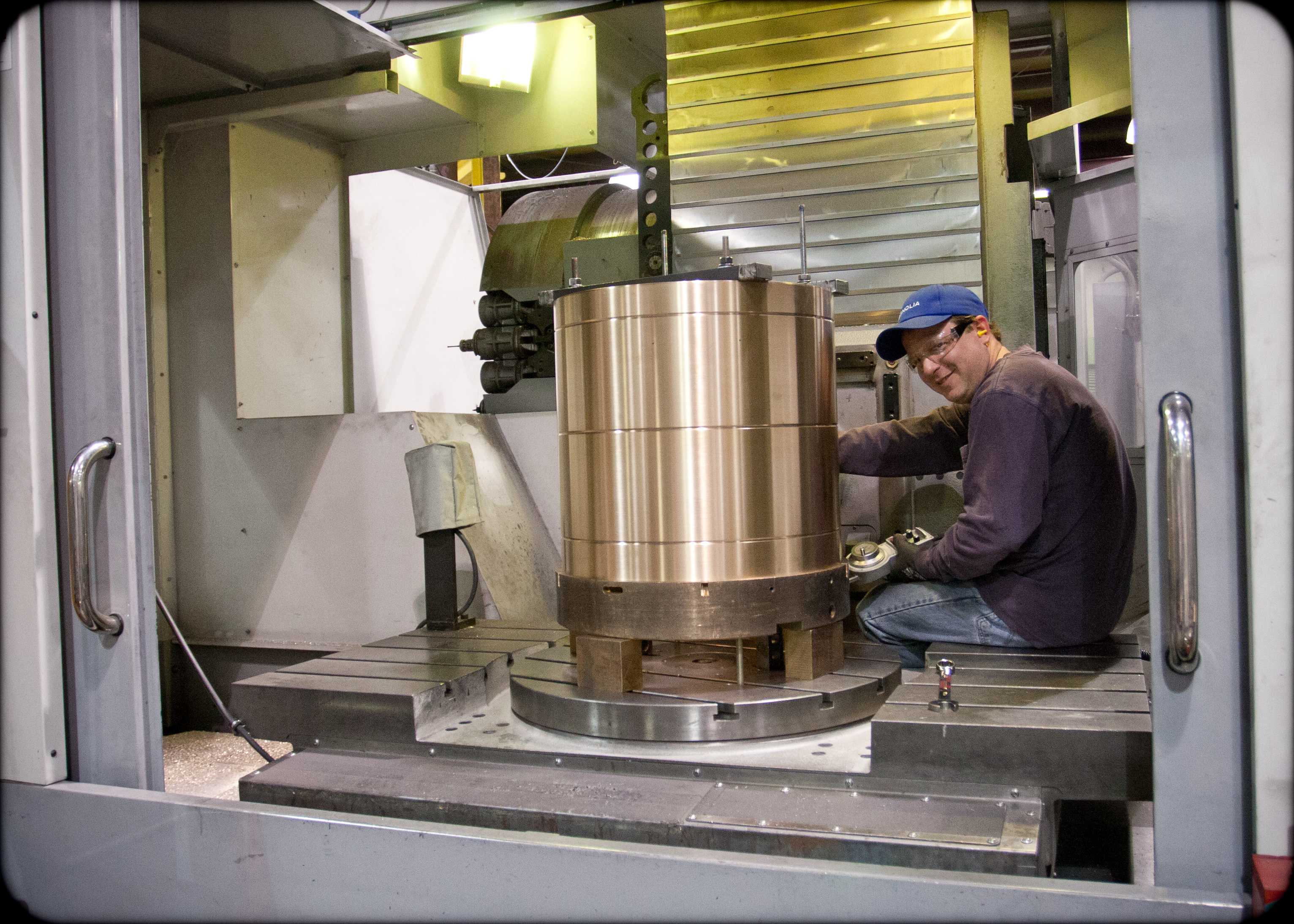 Machinist inside a CNC machining center with a large bronze component secured on the machine table.