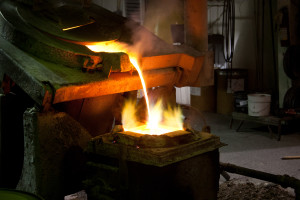 Tilting furnace pours molten metal into a mold, with flames visible at the mold opening.