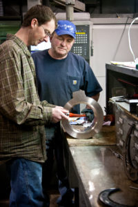 Two Magnolia Metal team members measure a large ring-shaped metal component in the machine shop.